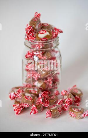 Un vasetto di vetro da muratore Ball trabocca di caramelle di Goetze (note anche come Bull's Eyes), un morbido caramello chewy con ripieno di crema Foto Stock