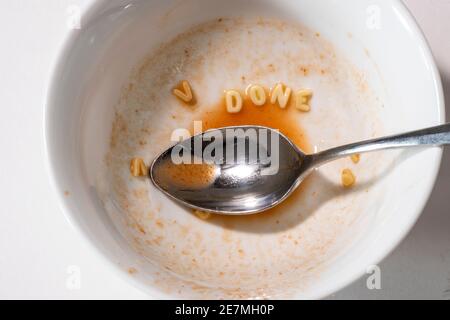 Un cucchiaio si siede in una ciotola quasi vuota di zuppa di alfabeto di pomodoro, i noodle scrivono "FINE". Studio su bianco. Foto Stock