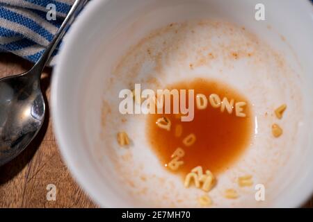 Un cucchiaio si siede accanto a una ciotola quasi vuota di zuppa di alfabeto di pomodoro, i noodle scrivono "FINE". Foto Stock