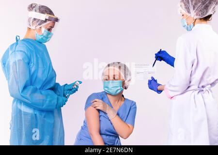 Un infermiere prepara una siringa con un vaccino per una giovane donna medico. E le danno un certificato di vaccinazione su sfondo bianco. Foto Stock