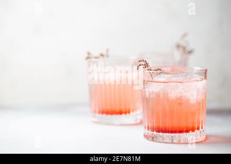 Bevanda fresca fresca di limonata rosa con ghiaccio in un bicchiere su sfondo bianco, fuoco selettivo Foto Stock