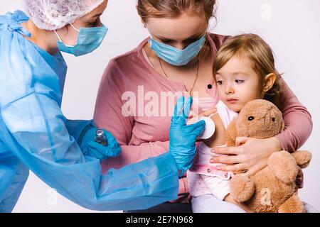 La mamma tiene il bambino tra le braccia e si calma dopo la vaccinazione. Il medico mette un batuffolo di cotone sul sito di iniezione. Sfondo bianco. Foto Stock