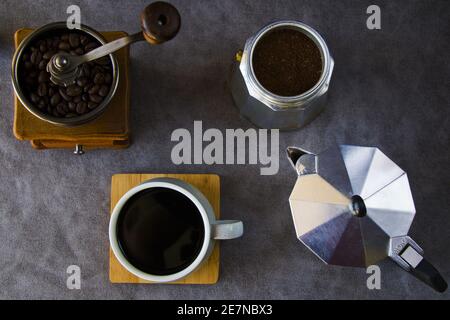 Vista dall'alto di una macchina per il caffè, un macinacaffè e una tazza di caffè su sfondo grigio Foto Stock