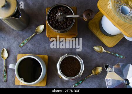 Vista dall'alto di macchine per il caffè, macinacaffè e una tazza di caffè su sfondo grigio Foto Stock