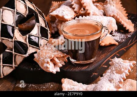 Cibo di Carnevale TIPICO, maschera e caffè aromatico su sfondo boscoso. Sfrappole o chiachiere o ali d'angelo. Pasta dolce tradizionale fritta e cosparsa di zucchero in polvere. Foto Stock