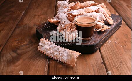 Cibo di Carnevale caffè TIPICO e aromatico su sfondo boscoso. Sfrappole o chiachiere o ali d'angelo. Pasta dolce tradizionale fritta e cosparsa di zucchero in polvere. Foto Stock