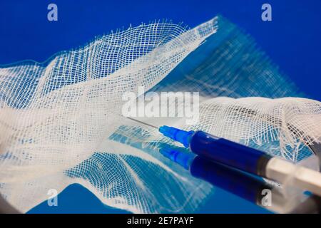 Una siringa medica e bendaggio sulla superficie dello specchio, sfondo blu. Controllo pandemico del coronavirus e protezione medica. Foto di alta qualità Foto Stock