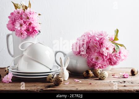 Concetto di Pasqua di primavera. Tazze bianche e teiera, fiori di ciliegio rosa, uova di quaglia su un tavolo di legno. Primavera ancora vita. Foto Stock