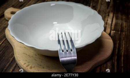 Un piatto vuoto con una forchetta su un vassoio di legno, un piatto senza cibo. Foto Stock