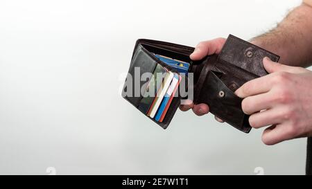 Un uomo guarda in un portafoglio vuoto senza soldi, un portafoglio con carte di credito. Su sfondo bianco. Foto Stock