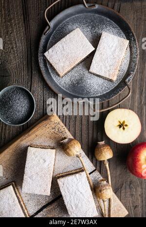 Deliziosa torta di pasta lievitata con semi di papavero e ripieno di mela, cosparsa di zucchero in polvere su rustico fondo di legno Foto Stock