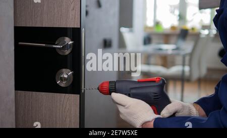 Un falegname installa una porta interna in un appartamento, un handyman perfora una serratura della porta, un giovane uomo effettua riparazioni in un appartamento. Foto Stock