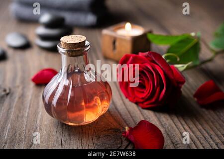 Acqua di rosa infusa fresca fatta in casa in una bottiglia di vetro per routine di cura della pelle su sfondo rustico di legno Foto Stock