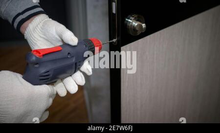 Il caposquadra effettua lavori di riparazione nell'appartamento, perfora la serratura della porta, l'uomo ripara la porta interna. Foto Stock