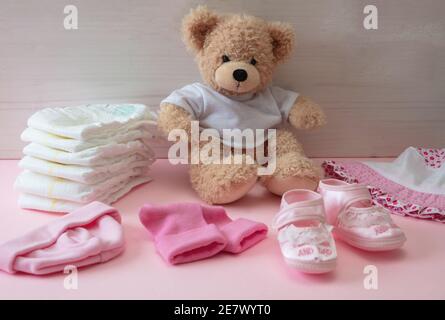 Accessori per bambina. Carino orsacchiotto seduto su pavimento di colore rosa, sfondo di legno muro. Forniture per bambine, pannolini, scarpe, abbigliamento Foto Stock