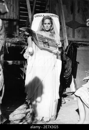 URSULA ANDRESS in costume come Ayesha legge quotidiano Daily Mirror mentre si riposa su Costume Board durante la pausa nelle riprese di LEI 1965 regista ROBERT DAY basato sul romanzo di H. Rider Haggard Hammer Films / Warner - Pathe Distributori Foto Stock