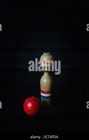 Una singola spina da bowling in legno in piedi in verticale accanto a un rosso sfera Foto Stock