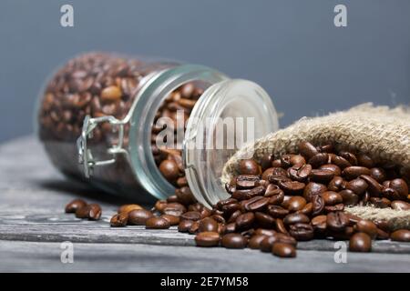 Chicchi di caffè. Versate in un vasetto di borsa di trascinamento e in una borsa di lino. La banca è ribaltata. Primo piano. Foto Stock