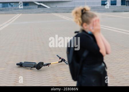 Ragazza seduta piangendo dopo che è caduto mentre cavalcava il suo scooter sulla strada della città Foto Stock