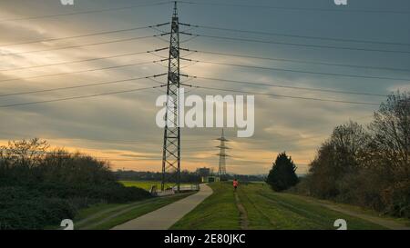 I tralicci di elettricità sono sparsi fuori nel campo mentre un jogger corre lungo una diga al tramonto Foto Stock