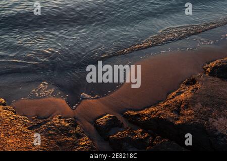 spiaggia all'alba, ora d'oro con calmo, oceano blu e riflesso del sole sulle rocce della spiaggia Foto Stock