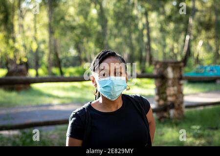 Bel ritratto di donna africana che indossa una maschera blu usa e getta all'esterno. Foto Stock