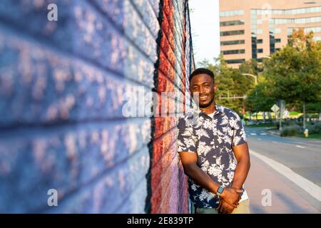 Un uomo nero si appoggia contro un colorato murale di strada e sorride alla telecamera. Foto Stock