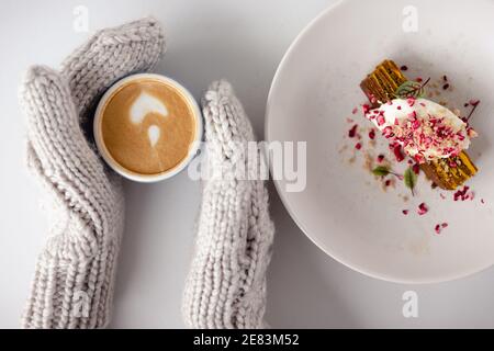 le mani mitte delle donne tengono una tazza di caffè e una torta accanto ad essa su un tavolo bianco da vicino. Vista dall'alto. Sfondo di Natale. Concetto di inverno, calore, h Foto Stock