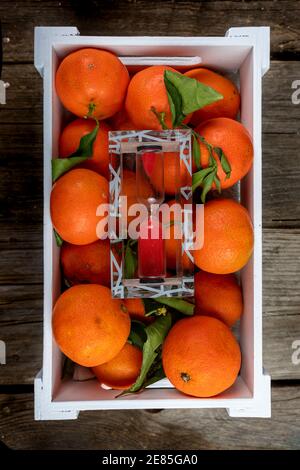 scatola bianca piena di tangerini e una clessidra sopra uno sfondo di legno Foto Stock