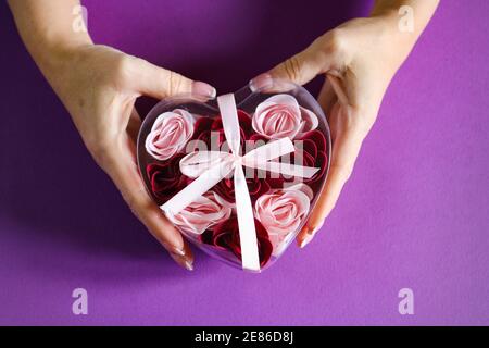 Mani che tengono una scatola a forma di cuore sullo sfondo viola Foto Stock