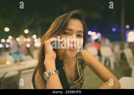 Chiusura del giovane bella donna asiatica parlando al telefono cellulare mentre il raggrinzimento labbra al mercato notturno di Hua Hin in Thailandia Foto Stock