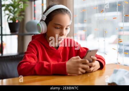 Foto di una ragazza adolescente in una cuffia bianca durante le chat online con gli amici. Concetto di tecnologia moderna. Foto Stock