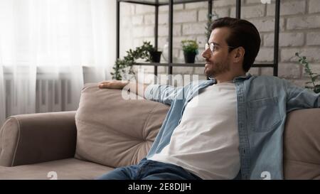 Primo piano uomo sognante che guarda da parte, rilassandosi sul divano Foto Stock