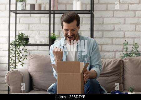 Uomo sopravorato che indossa occhiali guardando in scatola di cartone, pacco ricevuto Foto Stock