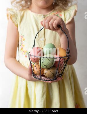 bambina in un vestito giallo che tiene il cesto con pastello Uova di Pasqua Foto Stock