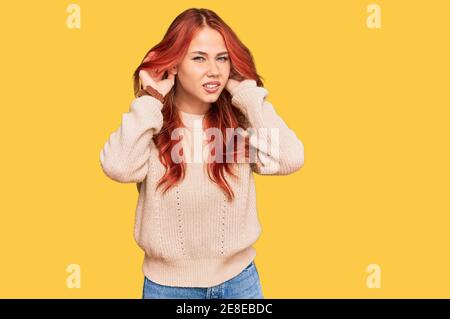 Giovane donna rossa che indossa un maglione invernale casual cercando di sentire entrambe le mani sul gesto dell'orecchio, curiosa per pettegolezzi. Problemi di udito, sordi Foto Stock