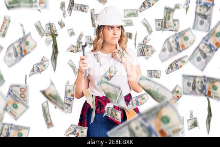 Giovane donna caucasica che indossa hardhat che tiene la chiave faccia seria che pensa alla domanda con la mano sul mento, pensieroso circa idea confusa Foto Stock