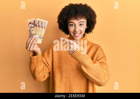 Giovane ragazza ispanica che tiene 5000 banconote forint ungheresi sorridenti felici puntare con la mano e il dito Foto Stock