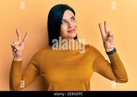 Giovane donna caucasica che fa la vittoria segno positivo gesto sorridente guardando al lato e fissando via pensare. Foto Stock