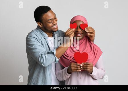 Ragazzo nero amorevole che copre gli occhi della sua ragazza con carte valentine Foto Stock