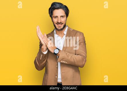 Giovane uomo ispanico che indossa abiti da lavoro aggrappando e applaudendo felice e gioioso, sorridendo mani orgogliose insieme Foto Stock