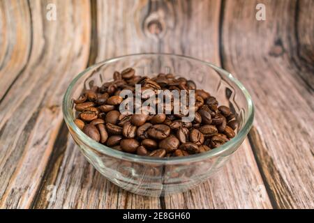 I chicchi di caffè appena tostati si trovano in un vaso di vetro trasparente su un tavolo di legno Foto Stock