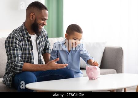 Padre africano e Figlio che mette il risparmio personale in Piggybank Indoor Foto Stock