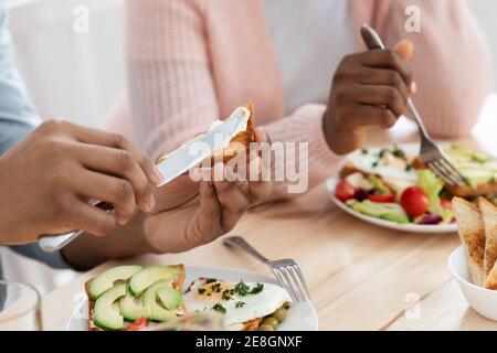 Ora della colazione. Irriconoscibile coppia afroamericana gustando cibo gustoso in cucina Foto Stock