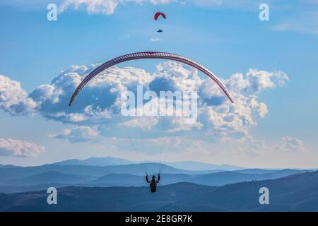 Incontro in aria sotto le nuvole. Un parapendio sta andando dritto. L'altro sta volando sopra il suo arco. Parapendio a Goriska. Slovenia Foto Stock