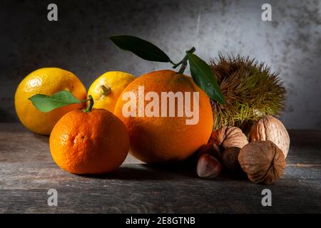 Autunno ancora vita di citrus e noci. Macro Foto di Tangerina arancione e due limoni con tre noci, nocciola e castagno. Su tavola di legno con Foto Stock