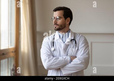Il medico maschile pensivo guarda a distanza pensando Foto Stock