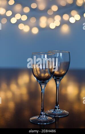 Bicchieri di vino vuoti su un tavolo di vetro con fondo bokeh primo piano. Capodanno, Natale umore. Biglietto d'auguri. Concetto di festa e festa. Foto Stock