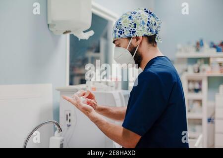 Vista laterale del medico maschile non riconoscibile nella maschera respiratoria e. disinfezione uniforme delle mani in ospedale Foto Stock