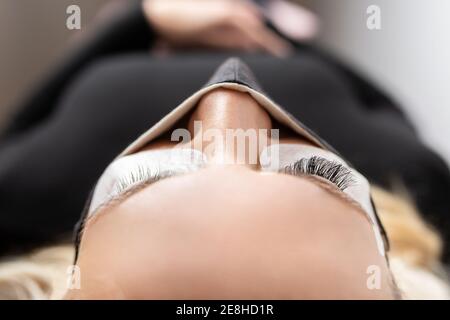 Dettaglio delle ciglia artificiali su giovane cliente femminile indossando protettivo maschera in moderno studio di bellezza Foto Stock